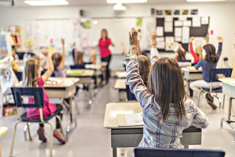 children raising their hands in a classroom with a teacher at the front