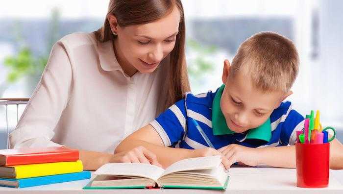 a teacher and a young boy are surrounded by books at a table as the young boy writes