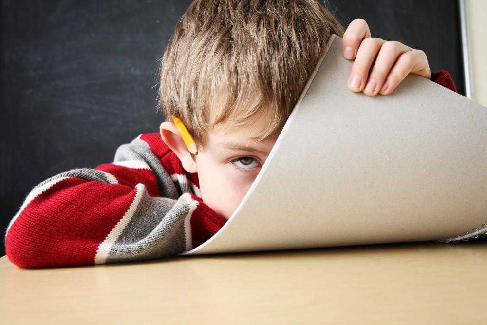 child with a pencil in his ear hiding behind a notebook