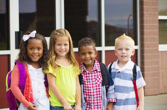 four children smile for the camera with backpacks on