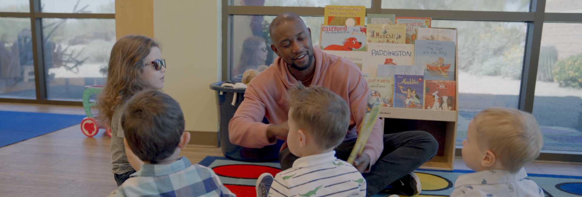 a male teacher reads to a group of children on the floor