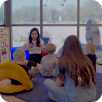 an icon of teachers reading to children on the floor while two teacher supervise from the back