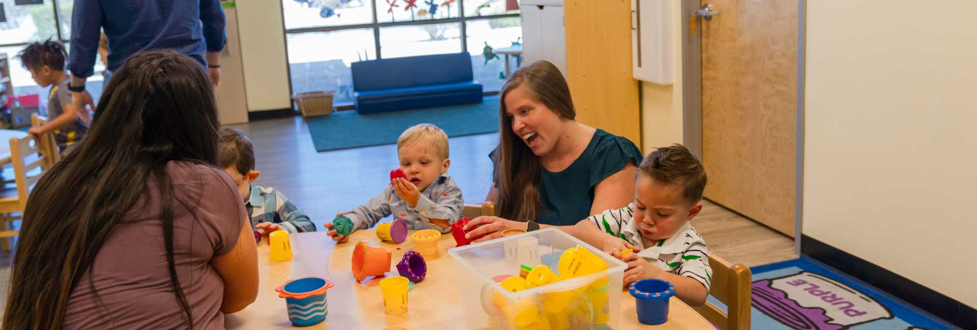 two teachers play with children at a table with toys