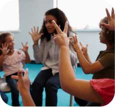 a teacher and children hold up their hands signaling numbers