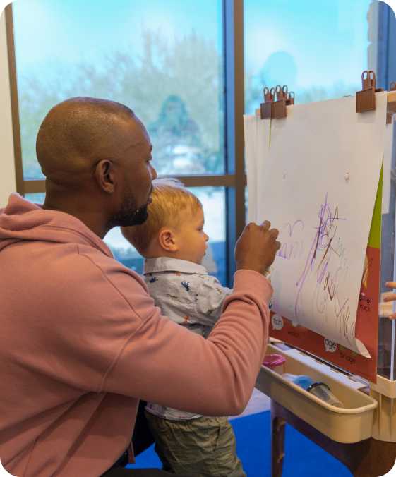 a man and a child draw on a piece of paper on an easel