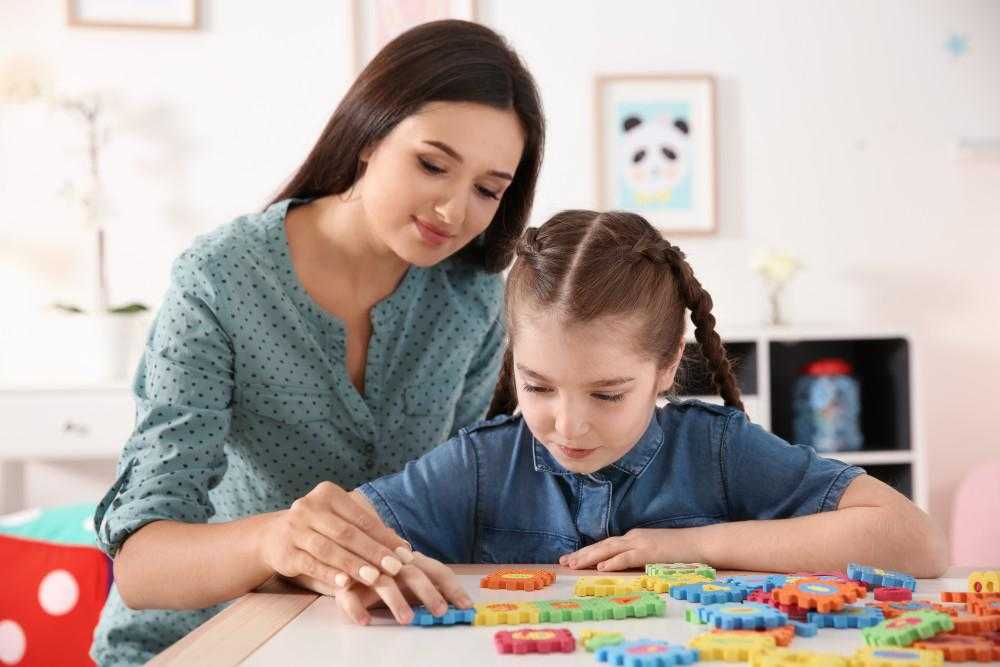 a female teacher and a young girl play with puzzle toys at a table