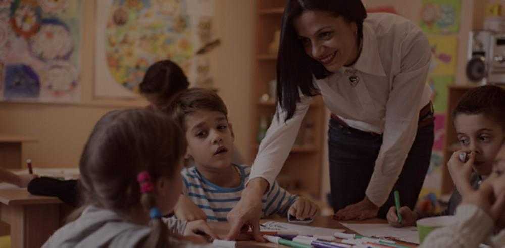 teacher points towards something on table while children sit around the table