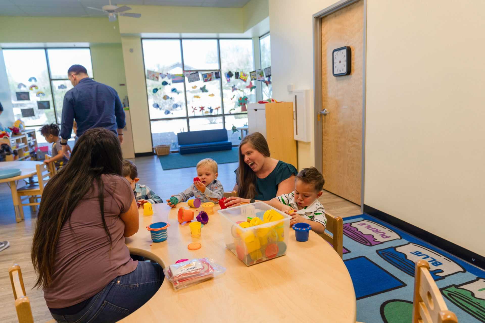 two teachers play with 2 kids at a table with toys